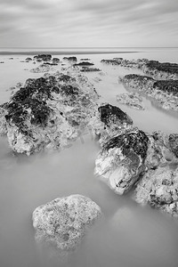 美丽的黑白长曝光日出时有岩石的低潮海滩风景图片