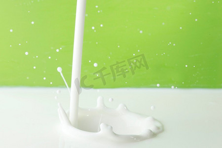 倒牛奶水花。在绿色背景上倒牛奶飞溅的特写镜头