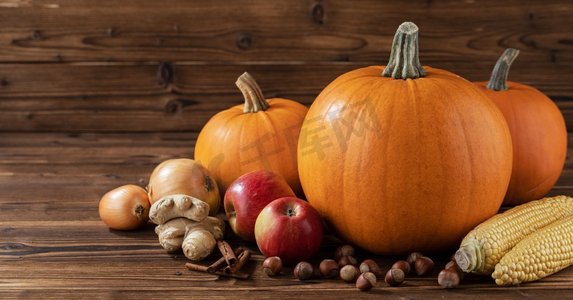 秋收背景摄影照片_秋收静物，木质背景上有南瓜、苹果、榛子、玉米、生姜、洋葱和肉桂。木桌上的秋收
