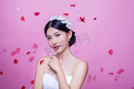 肖像美丽的新娘与玫瑰花瓣在半空中反对粉红色背景