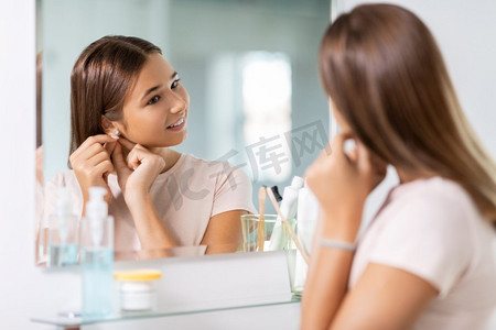 美丽、卫生和人的概念-戴着钻石耳环的十几岁女孩在浴室照镜子。戴着耳环照镜子的少女