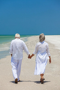 后视图老年男女夫妇手牵手走在热带海滩