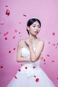 美丽的新娘举着玫瑰花瓣站在粉色的背景下