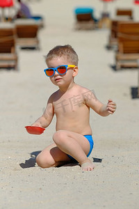 玩沙子摄影照片_两岁的学步男孩在海滩上玩铲子和沙子