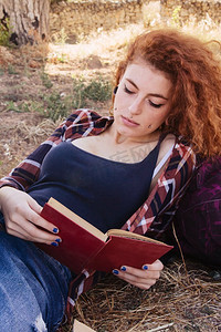 年轻的红发女子阅读户外 