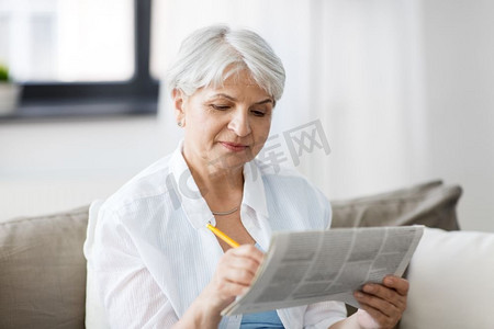 老报纸摄影照片_年龄和人的概念—老年妇女在家中标记报纸广告。老年妇女在家中标记报纸广告