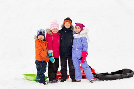 童年、友谊和季节概念-一群快乐的小朋友在冬天拉着雪橇拥抱。冬天抱着雪橇的快乐小朋友