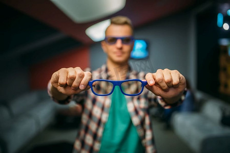 放映前，一名男性观众在电影院大厅展示3D眼镜。电影院里的男人，娱乐生活方式