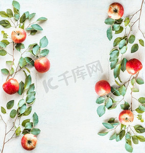 树叶边框树枝边框摄影照片_框架由红苹果和绿色树枝组成，白色书桌背景上有树叶。俯视图。平躺着。苹果的边框。食品布局背景
