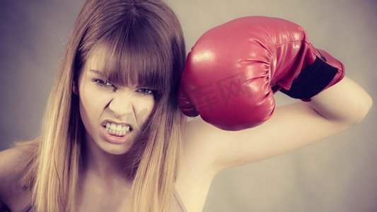 红色励志摄影照片_穿着红色拳击手套的运动女，正在打架。工作室拍摄灰色，背景。戴拳击手套的女人