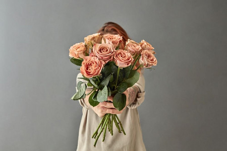 一个女人给一束米色玫瑰卡布奇诺，在灰色背景。母亲节，’一个女人给了一束米色玫瑰
