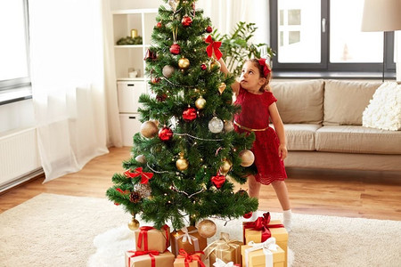寒假和人的概念—快乐的小女孩装饰圣诞树在家里。小女孩装饰圣诞树在家里