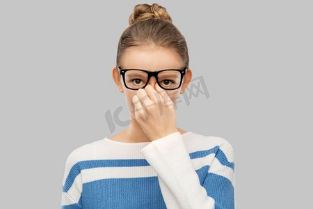 视力和人概念—眼镜的少女摩擦鼻梁在灰色背景十几岁的女孩在眼镜摩擦鼻梁