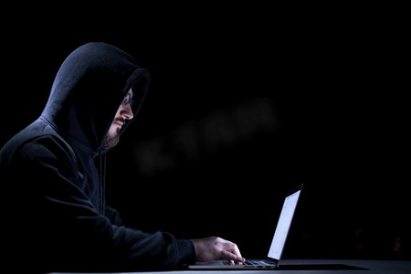 年轻有才华的黑客使用膝上型计算机，而在黑暗的办公室工作与大城市灯在背景在晚上