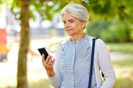 技术，老年和人的概念—愉快的高级妇女与智能手机在夏季公园。快乐的高级妇女与智能手机在夏季公园