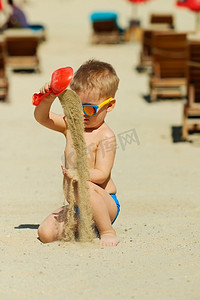 蹒跚学步的男孩在沙滩上玩铲子和沙子。2岁的蹒跚学步的男孩在海滩上玩铲子和沙子 