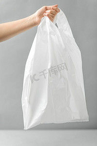 消费主义和生态友好的概念—妇女拿着白色一次性塑料袋在灰色背景。妇女拿着白色一次性塑料袋