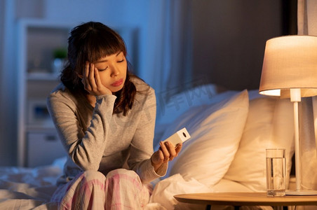 人、睡觉时间和休息观念-压力很大的亚洲女性晚上在床上打卡。亚洲女人晚上坐在床上带着闹钟