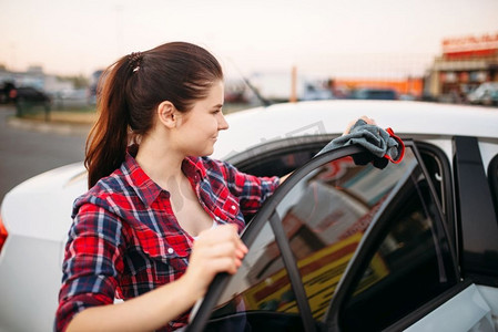 妇女在自助洗车机上清洗后擦拭汽车。女士清洁车