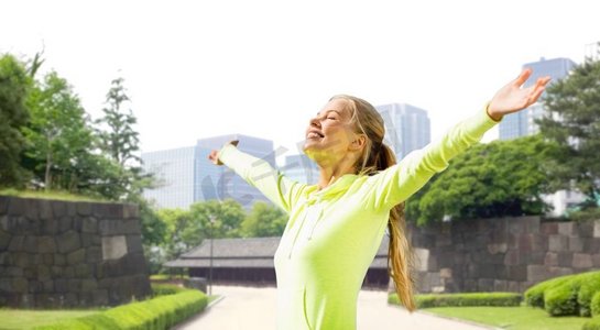 健身背景摄影照片_健身，运动和健康的生活方式概念—运动衣服享受太阳在城市公园背景的快乐妇女快乐的女人在运动服