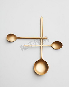 一个创造性的组成不同的金勺子在灰色背景。俯视图。三个不同的金属勺子孤立在灰色背景