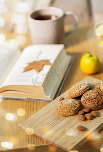hygge，烘焙和食品概念—燕麦饼干，杏仁，书和茶在木桌子在家里。燕麦饼干，杏仁和书在家里的桌子上