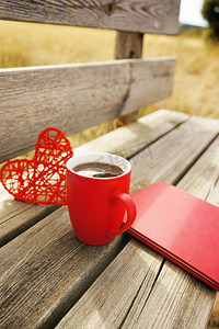红色的的心摄影照片_早上在户外的木凳上放着一杯红色的杯子和咖啡