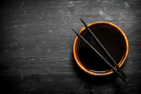 酱油在碗和筷子里。在一个黑色的木背景。酱油在碗和筷子里。