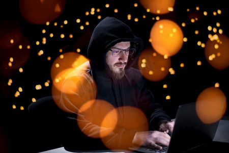 年轻有才华的黑客使用膝上型计算机，而在黑暗的办公室工作与大城市灯在背景在晚上
