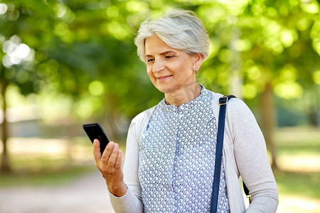 技术，老年和人的概念—愉快的高级妇女与智能手机在夏季公园。快乐的高级妇女与智能手机在夏季公园