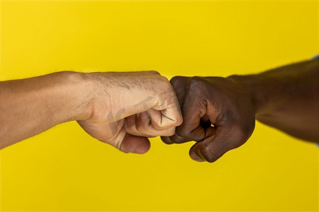 前景欧洲人和非洲人的手到手紧握成拳头在黄色背景
