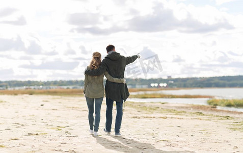 爱情、关系和人情观--一对微笑的情侣走在秋天的海滩上拥抱着。一对情侣沿着秋天的海滩散步，拥抱着