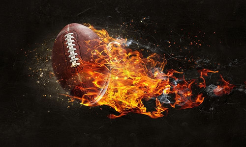 火焰足球摄影照片_橄榄球在黑暗的背景下燃烧起来。混合媒体。美式足球比赛的概念。混合介质