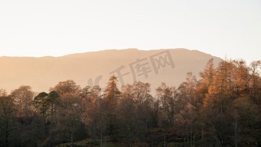 落叶松和松树的美丽风景映衬着夕阳的橙色光芒，远处的山脉在英国湖区