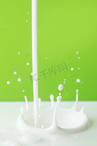 倒牛奶飞溅在绿色背景特写镜头。倒牛奶飞溅