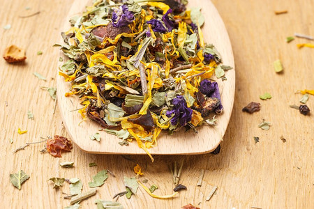 一堆混合的天然药用干药草叶和花瓣在木勺上。.一堆干燥的药草叶子和花瓣
