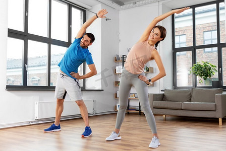 矢量健身器材摄影照片_运动，健身，生活方式和人们的概念—微笑的男人和女人在家里锻炼。快乐的夫妇在家里锻炼