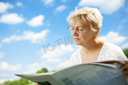 在天空的衬托下拿着报纸的老妇人