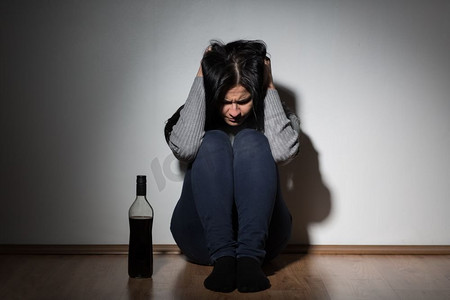 酗酒、抑郁和人们的观念--不快乐的女人拿着酒瓶在家中哭泣。拿着酒瓶的女人在家中哭泣