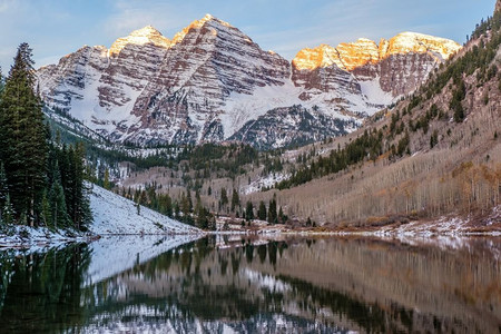 美国科罗拉多州秋天的黎明时分，栗色的钟声和栗色的湖水在雪地里倒映着岩石和山脉。