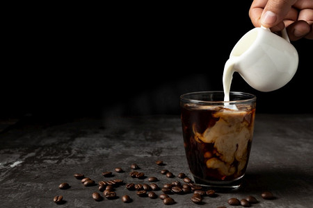 饮料摄影照片_牛奶倒进冰的黑咖啡在桌子和黑色背景。