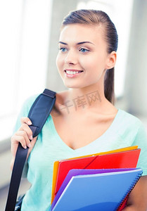 快乐的女学生背着书包和彩色文件夹。背着书包和彩色文件夹的女学生