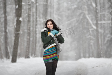 美丽的年轻女子穿着毛衣在公园的冬日散步。看着摄像机