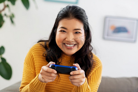 游戏手柄摄影照片_人和休闲概念—愉快的微笑的亚洲年轻妇女有游戏手柄玩视频游戏在家里亚洲妇女与游戏手柄玩游戏在家里