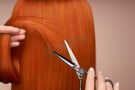 美发沙龙摄影照片_理发师用剪刀剪红色长发。美发沙龙，发型师。护发美发产品。染发
