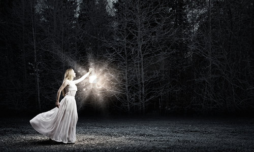 启示摄影照片_在黑暗中迷失。年轻女子与灯笼走在黑暗的森林