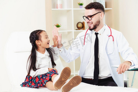 年轻的男医生在医院办公室检查小孩。孩子很高兴，不怕医生。儿童医疗保健概念。