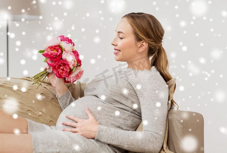 怀孕，人和节假日的概念--快乐的孕妇带着花在家中飘过雪。家有鲜花的快乐孕妇