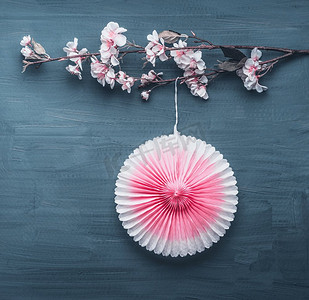 纸扇花背景摄影照片_春季装饰，人造春花树枝和粉色派对纸扇在灰蓝色背景上，俯视