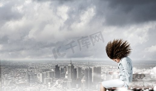 商业上的挑战。一位年轻的女商人坐在楼顶上，一头飘动的头发